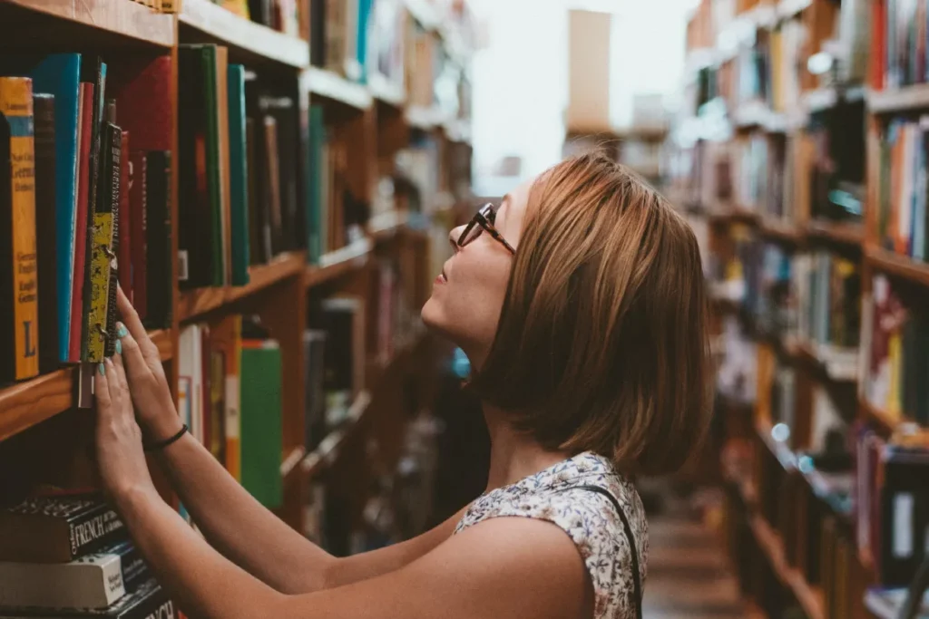 A woman reaching for a book on a library shelf